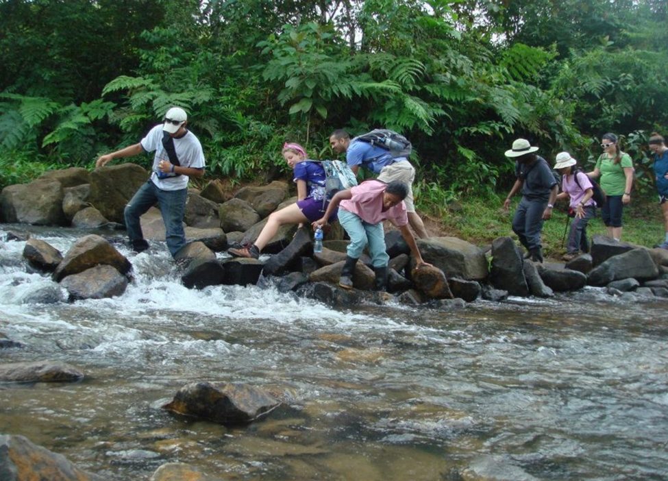 ISL volunteers helping one another cross a rocky river on the trail to a remote village